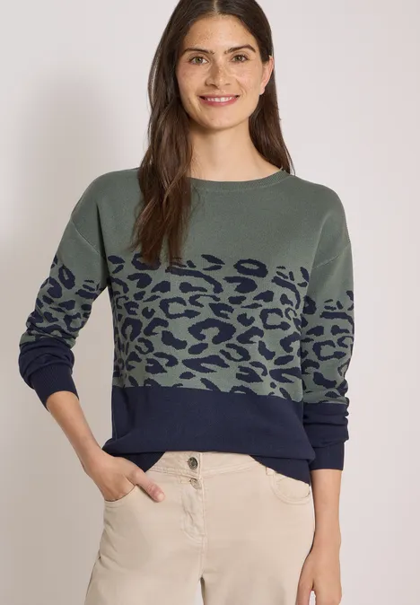 Frau trägt grünen Pullover mit dunkelblauem Leopardenmuster und heller Hose