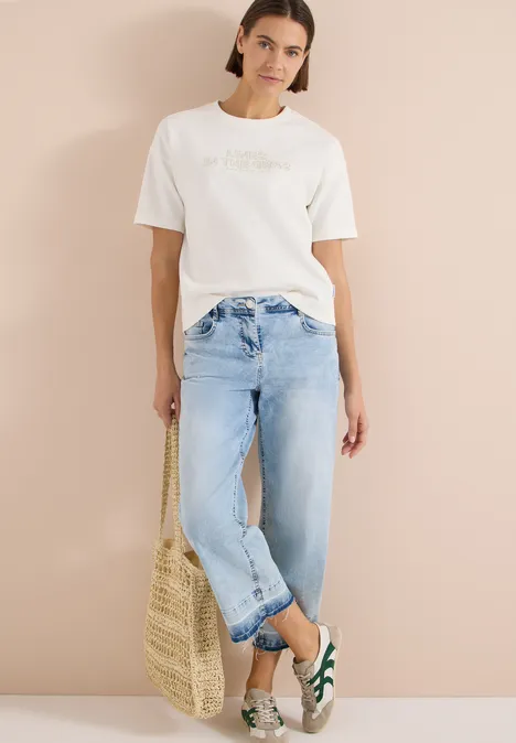 Vrouw met wit T-shirt, lichtblauwe jeans, groen-witte schoenen en strozak voor een beige achtergrond.