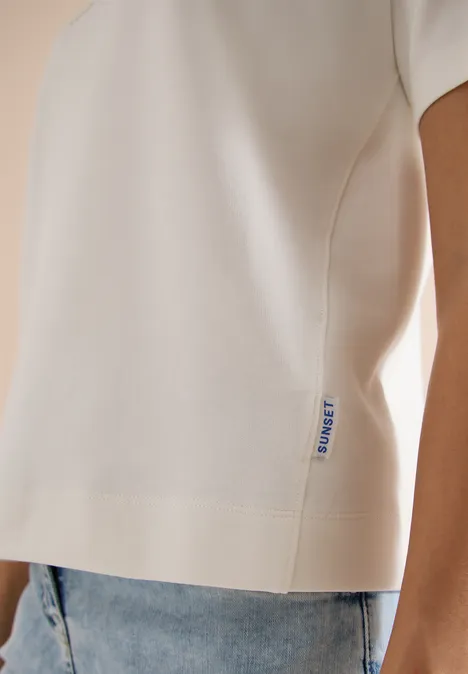 Zijdetail van een witte korte mouwen top met klein label, gecombineerd met lichtblauwe jeans.