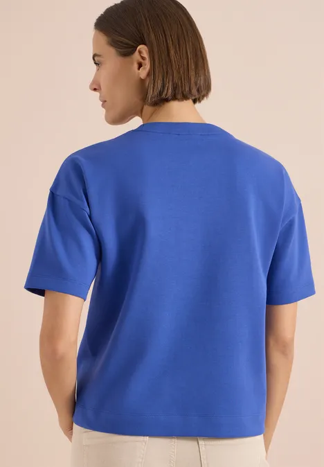 Een vrouw van achter draagt een blauw T-shirt met korte mouwen.