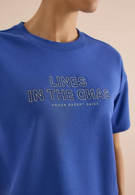Blauw T-shirt met opschrift 'LINES IN THE OPA?' en kleine tekst 'UNDER DESSERT SKIES'.