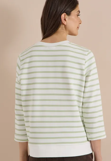 Top met groene en witte strepen, driekwart mouwen, gezien van achteren tegen crème achtergrond.