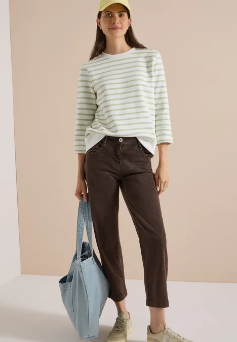 Vrouw in gestreept shirt, bruine broek, witte sneakers, pet en grote lichtblauwe stoffen tas