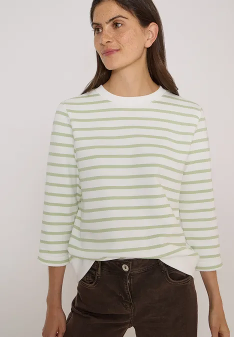 Vrouw draagt wit t-shirt met lichtgroene strepen en bruine corduroy broek.