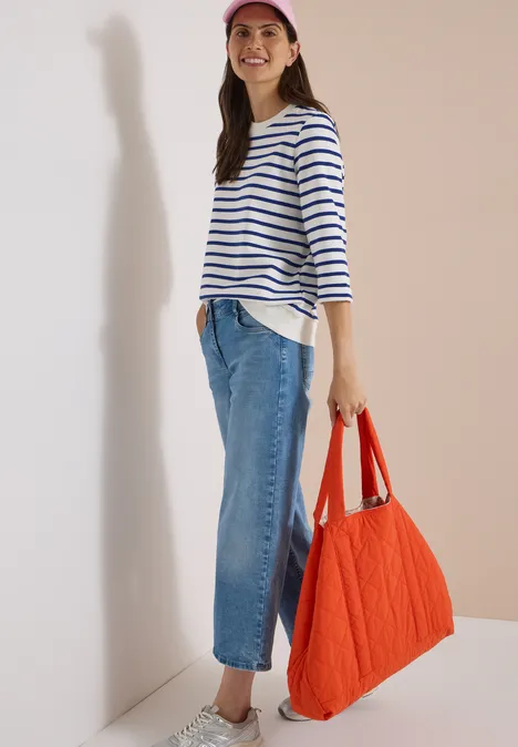 3/4-Arm Sweatshirt mit Rundhals und Streifen deep river blue Frau in Streifenshirt, Jeans und roter Tasche lehnt an weißer Wand und lächelt.