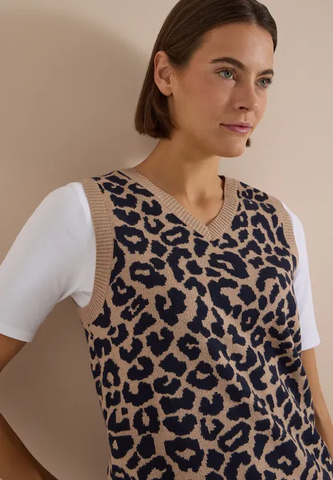 Frau trägt V-Ausschnitt-Strickweste mit braun-schwarzem Leopardenmuster über weißem T-Shirt.