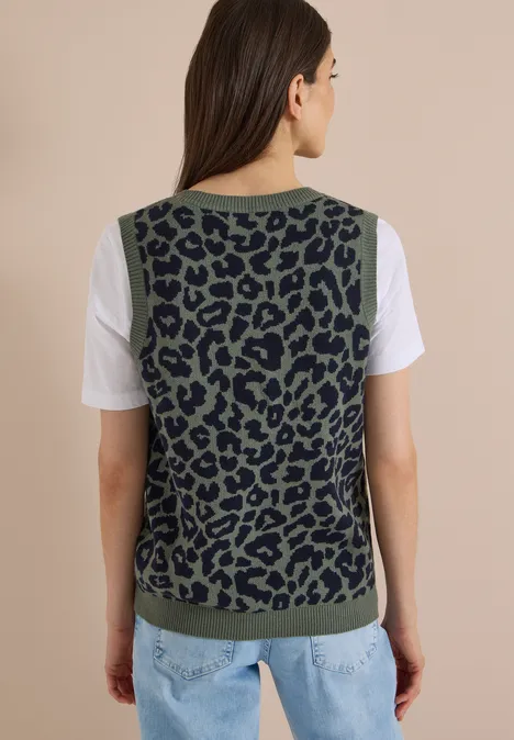 Frau von hinten mit khakigrün-schwarzer, leopardgemusterter Strickweste über T-Shirt und Jeans.