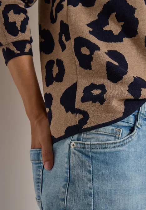 Person in beige-blauem Pullover mit Leopardenmuster und hellblauen Jeans, Hand in Tasche gesteckt