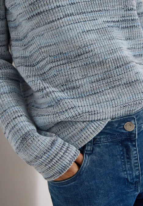 Person trägt hellblauen Strickpullover und steckt Hand in Vordertasche einer blauen Jeans.