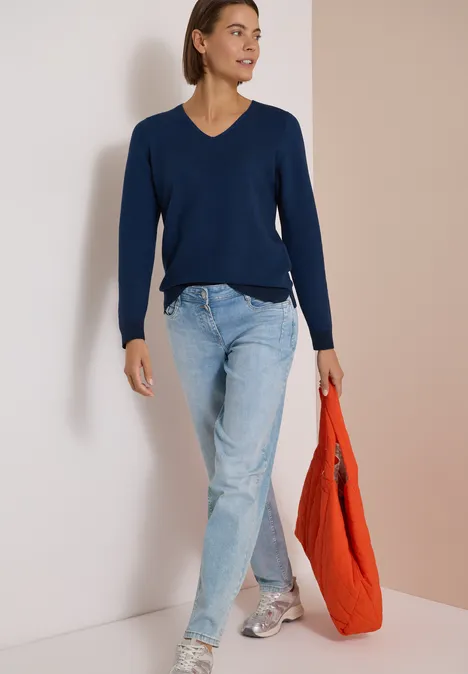 Pull bicolore à col en V urban dark blue Femme en pull bleu marine à col V, jean clair et baskets, portant un sac orange.