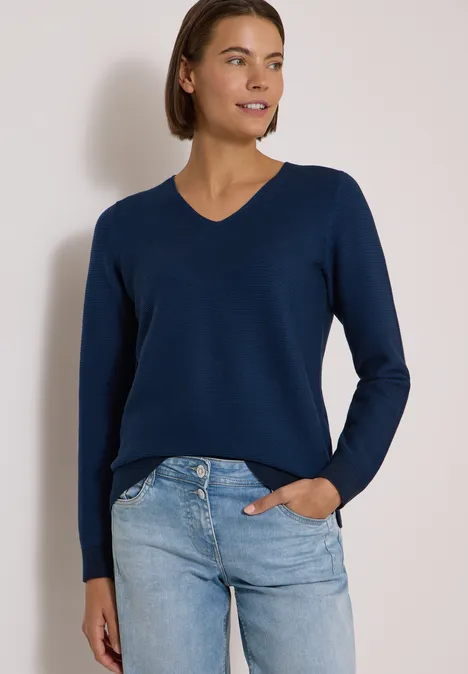 Pull bicolore à col en V urban dark blue Femme en pull bleu marine à col en V et jean clair, souriant devant un fond neutre.