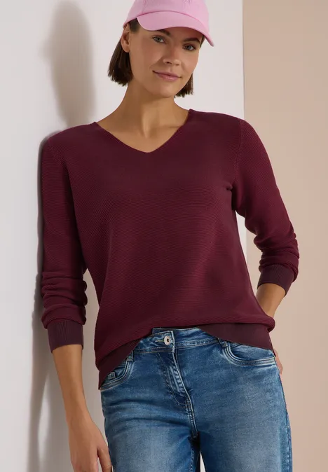 Pull bicolore à col en V berry red Femme en jean, pull bordeaux et casquette rose.