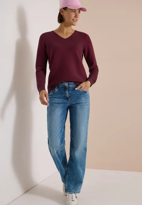 Pull bicolore à col en V berry red Femme casquette rose, pull framboise, jean large et baskets blanches appuyée contre un mur.