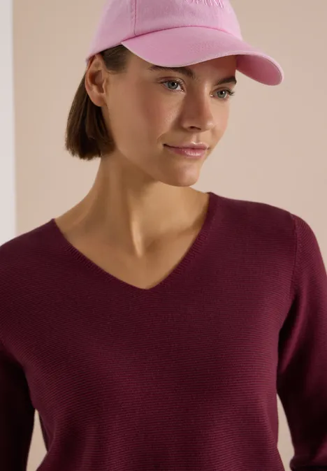 Pull bicolore à col en V berry red Femme portant une casquette rose et un pull bordeaux à col V.