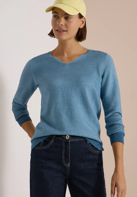 Pullover im Two-Tone-Look mit V-Neck mountain air blue Frau mit gelber Baseballkappe, blauem V-Pullover und dunklen Jeans.