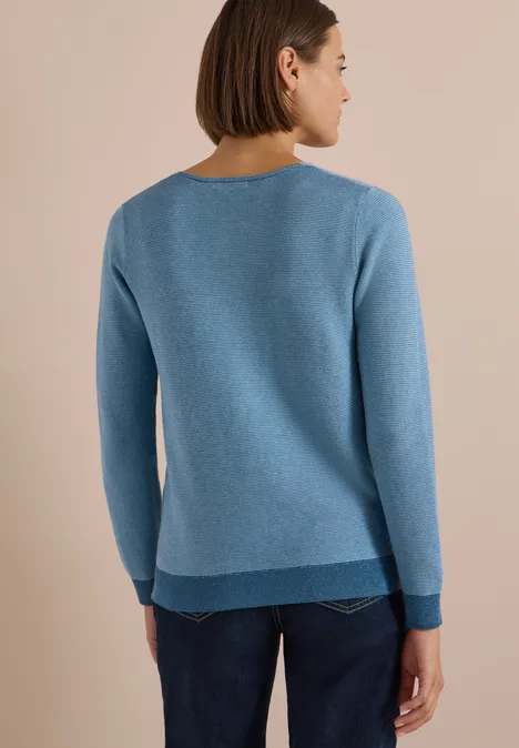 Pullover im Two-Tone-Look mit V-Neck mountain air blue Rückenansicht einer Frau in hellblauem Pullover und Jeans vor beigem Hintergrund.