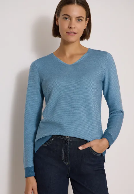 Pullover im Two-Tone-Look mit V-Neck mountain air blue Frau im blauen V-Pullover und Jeans vor weißem Hintergrund, eine Hand in der Hosentasche.