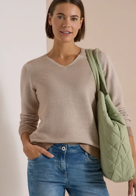Pull bicolore à col en V creamy mocha melange Femme en pull beige et jean bleu, portant un grand sac vert matelassé, souriante.
