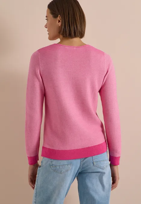 Eine Frau von hinten in pinkem Pullover und hellblauen Jeans vor neutralem Hintergrund.