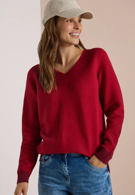 Pullover im Two-Tone-Look mit V-Neck flame red Frau in rotem V-Pullover, Jeans und Baseballcap lächelt seitlich.