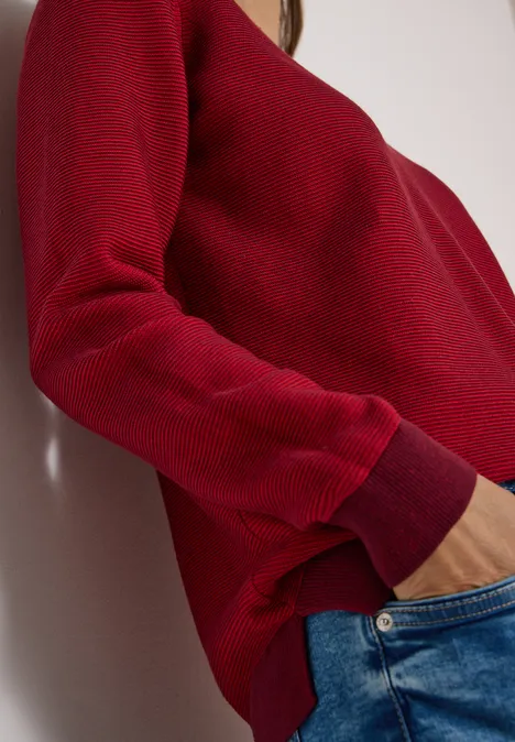 Pullover im Two-Tone-Look mit V-Neck flame red Seitliche Aufnahme einer Person in rotem Pullover und blauen Jeans mit Hand in Hosentasche.