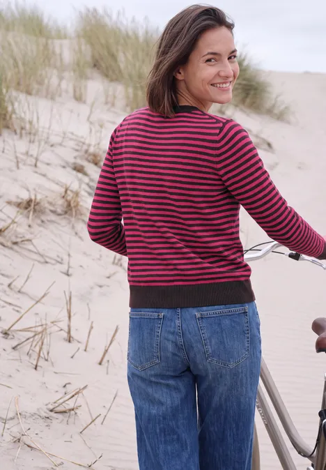 Trui met ronde hals en strepen pink flash melange Lachende vrouw op het strand naast haar fiets kijkt achterom.
