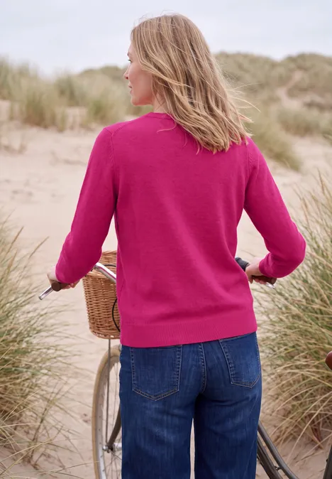 Effen trui met ronde hals pink flash melange Vrouw in roze trui en spijkerbroek duwt fiets langs zandduinen aan zee.