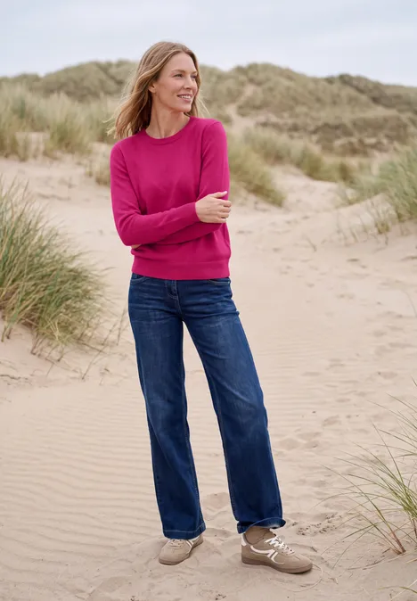 Effen trui met ronde hals pink flash melange Vrouw in roze trui en spijkerbroek lacht op zandduinen.