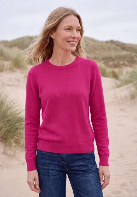 Effen trui met ronde hals pink flash melange Vrouw in roze trui glimlachend op een strand met duinen op de achtergrond.