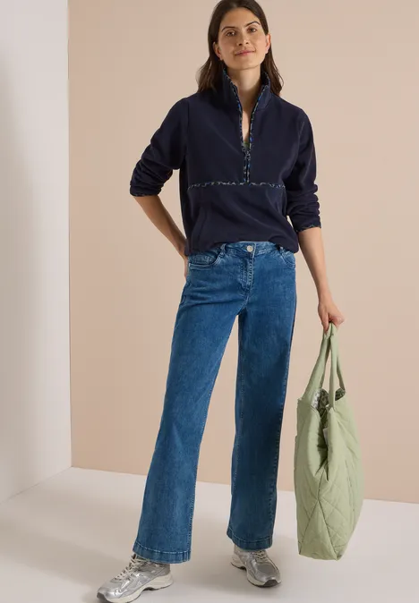 Fleecetrui met leopardetails urban dark blue Vrouw in donkerblau trui en jeans, draagt een lichtgroene tas van stof en glimlacht ontspannen.