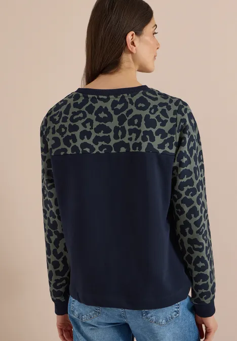 Vrouw in profiel, donkerblauwe trui met olijfgroene luipaardprint op mouwen en bovenrug.