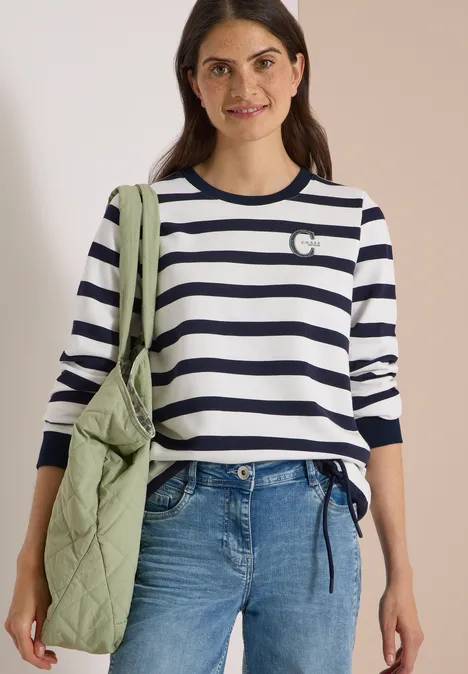 Sweatshirt mit Rundhals und Tunnelzug urban dark blue Frau mit dunkelblau-weiß gestreiftem Pullover, Jeans und grüner gesteppter Umhängetasche.