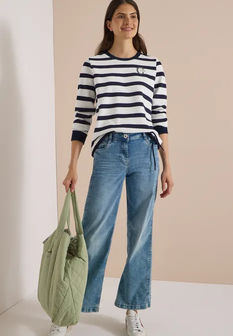 Sweatshirt mit Rundhals und Tunnelzug urban dark blue Frau trägt weiß-blau gestreiftes Shirt, weite Jeans, weiße Sneakers und hält eine grüne Stepp-Tragetasche.