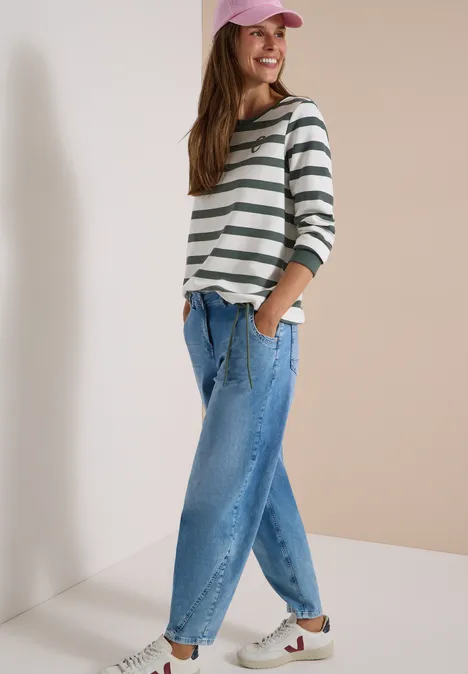 Eine lächelnde Frau trägt gestreiftes Shirt, Jeans und ein Cap