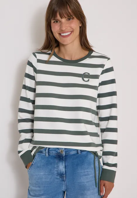 Frau lächelt, trägt weiß-grünes gestreiftes Langarmshirt mit Jeans.