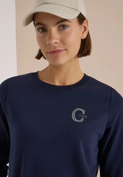 Frau mit hellgrüner Mütze trägt dunkelblaues Sweatshirt mit dezentem grünen C-Logo.