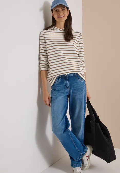 Sweatshirt mit Kapuze und Streifen natural taupe Frau lehnt an Wand, trägt gestreiftes Langarmshirt, Jeans, Baseballcap, weiße Sneaker und hält schwarzen Shopper.