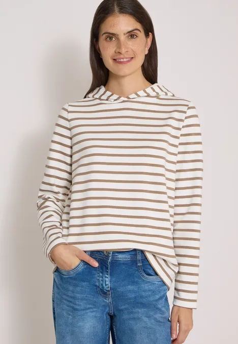 Sweatshirt mit Kapuze und Streifen natural taupe Frau in gestreiftem Langarmshirt (Weiß-Braun) und blauer Jeans, lächelt mit Händen in den Taschen.