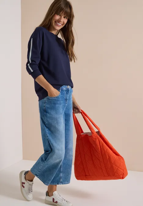Sweatshirt mit Rundhals und Tapedetails urban dark blue Eine Frau trägt einen dunkelblauen Pullover, weite Jeans, weiße Sneaker und hält eine große rote Tasche.