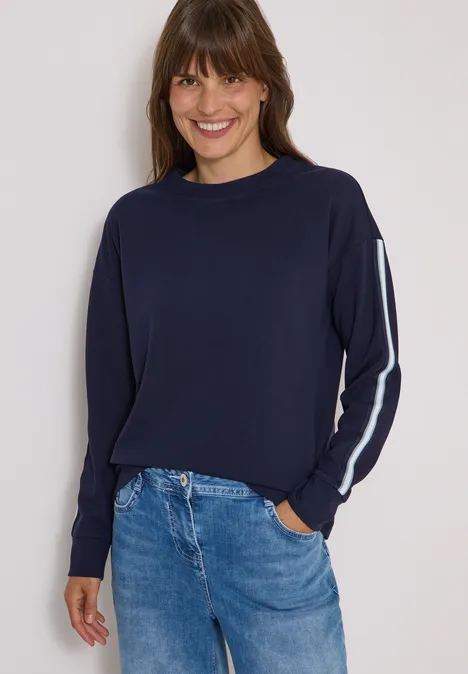 Sweatshirt mit Rundhals und Tapedetails urban dark blue Frau in dunkelblauem Pullover mit weißem Ärmelstreifen und Jeans, lächelnd.