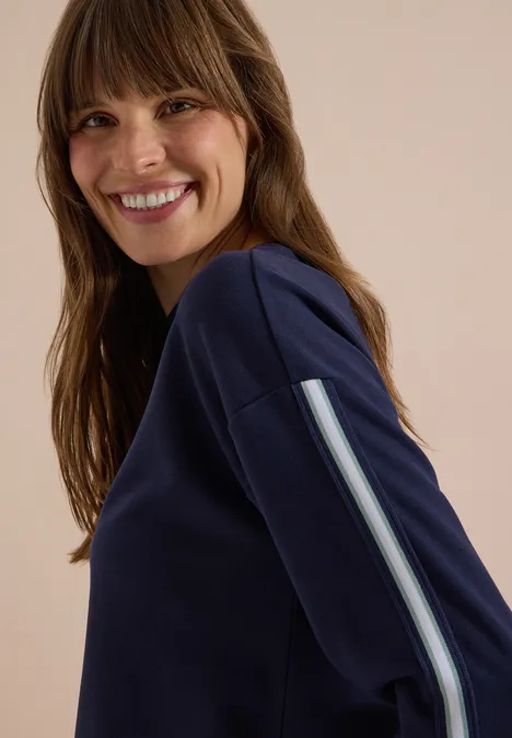 Sweatshirt mit Rundhals und Tapedetails urban dark blue Eine Frau in blauem Sweatshirt mit Streifen am Ärmel lächelt über die Schulter.