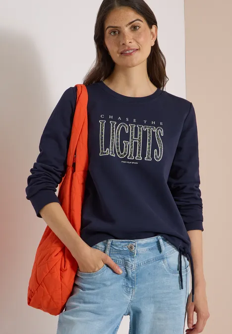 Sweatshirt mit Wording und Tunnelzug urban dark blue Frau mit dunkelblauem Sweatshirt ‚City Lights‘, heller Jeans und oranger Schultertasche lässig posiert.