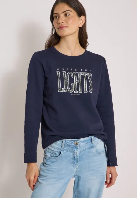 Sweatshirt mit Wording und Tunnelzug urban dark blue Frau in dunkelblauem Sweatshirt mit 'LIGHTS'-Schriftzug und hellblauen Jeans vor hellem Hintergrund.