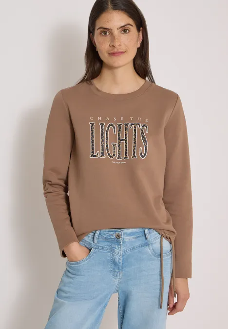 Sweatshirt mit Wording und Tunnelzug creamy mocha Eine Frau in braunem Sweatshirt mit Schriftzug ‘AMAZING LIGHTS’ und blauen Jeans vor hellem Hintergrund.