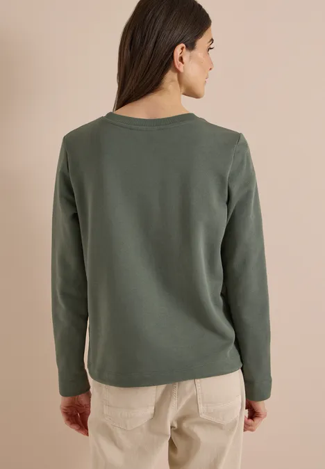 Sweatshirt mit Wording und Tunnelzug dried olive green Frau von hinten in olivgrünem Langarmshirt und beigen Hosen vor hellem Hintergrund.