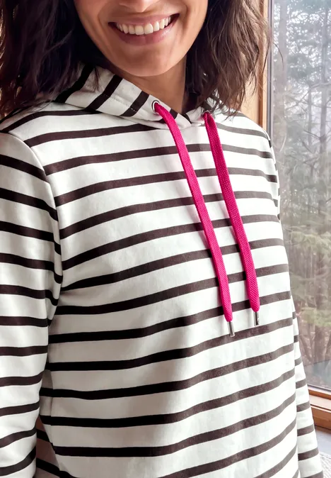 Sweat à capuche rayé truffle brown Gros plan d'une femme souriante en sweat rayé avec cordons roses.
