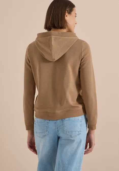 Sweatshirt mit Kapuze und Wording creamy mocha Frau von hinten, trägt beigefarbene Kapuzenjacke und hellblaue Jeans.