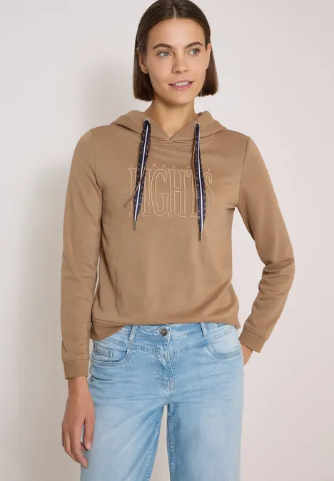 Sweatshirt mit Kapuze und Wording creamy mocha Junge Frau in beigem Hoodie mit 'icon'-Aufdruck und hellblauen Jeans.