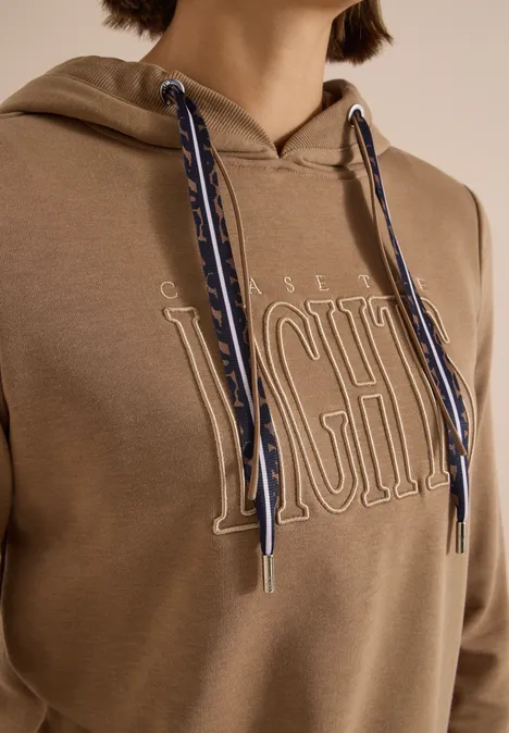 Sweatshirt mit Kapuze und Wording creamy mocha Beiger Kapuzenpullover mit großem 'LIGHT'-Schriftzug und blau-weißen gemusterten Kordeln.