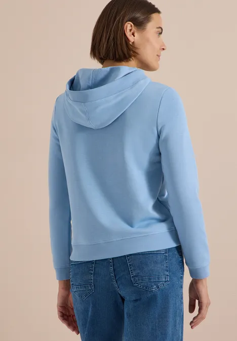 Sweatshirt mit Kapuze und Wording easy blue Eine Frau von hinten in hellblauem Hoodie und Jeans, Blick nach rechts.